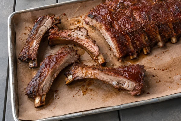 Smoked baby back ribs and sliced portions on a paper lined metal tray