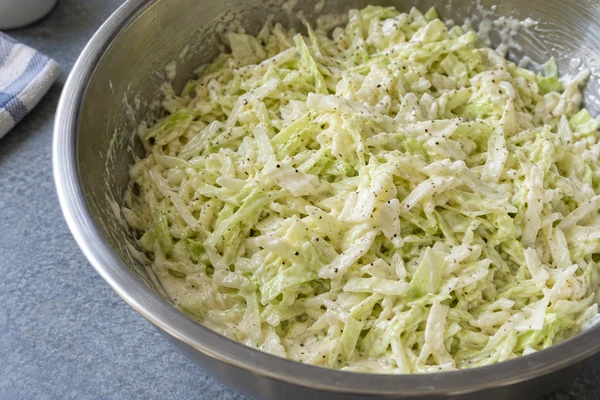 Creamy green cabbage slaw with black pepper in a stainless steel mixing bowl