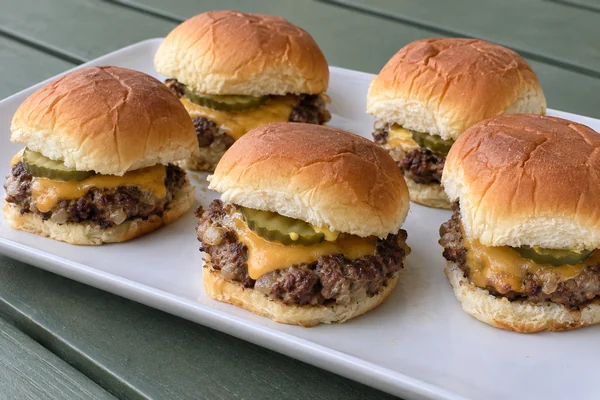 Small cheeseburgers with melted cheddar and pickles on sweet rolls